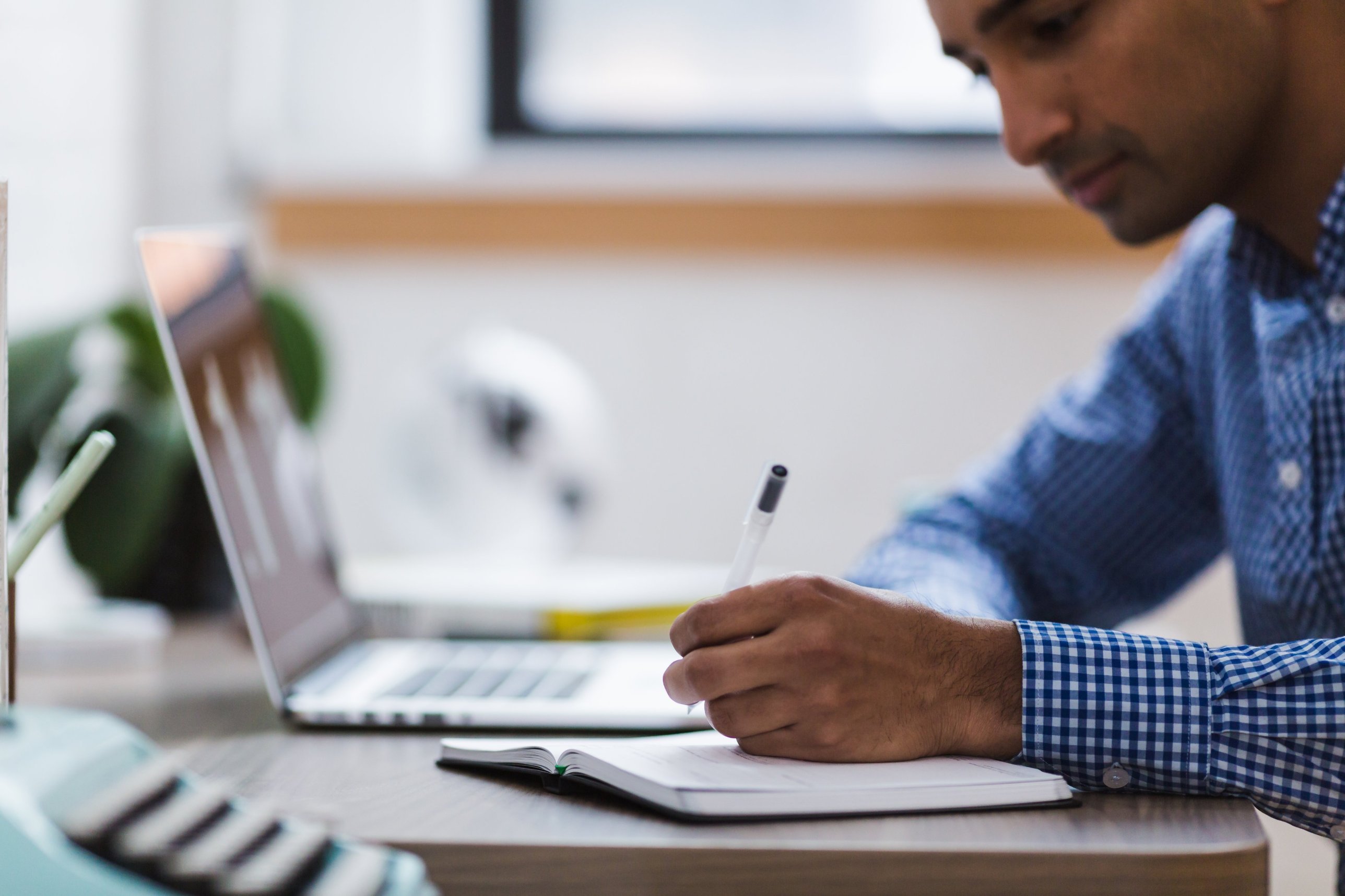 A man writing notes beside a laptop at a desk