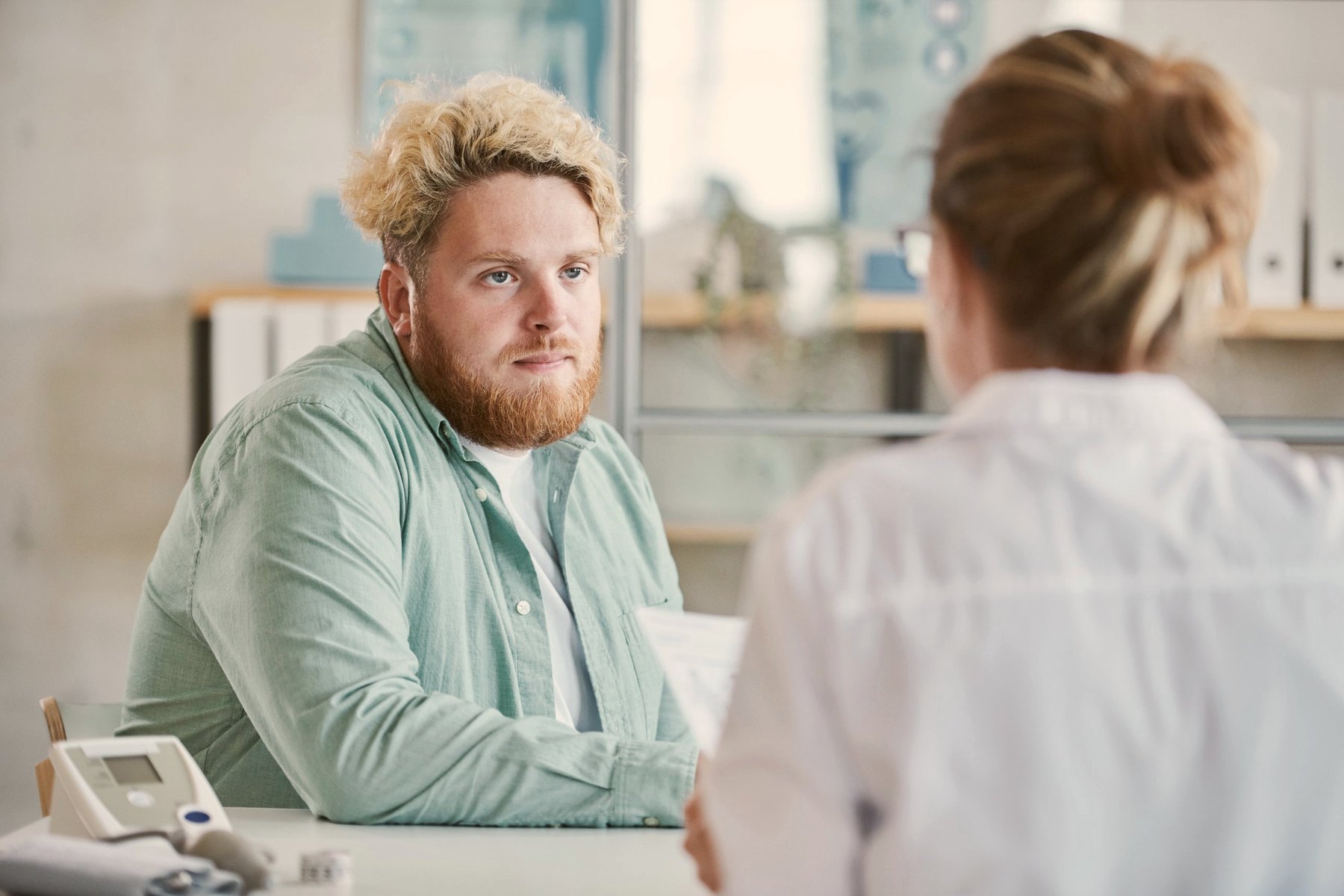 A man in a mint shirt listening to a clinician across a consultation desk