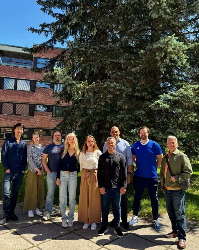 The Metabite team standing together outdoors in front of a brick building and a large spruce